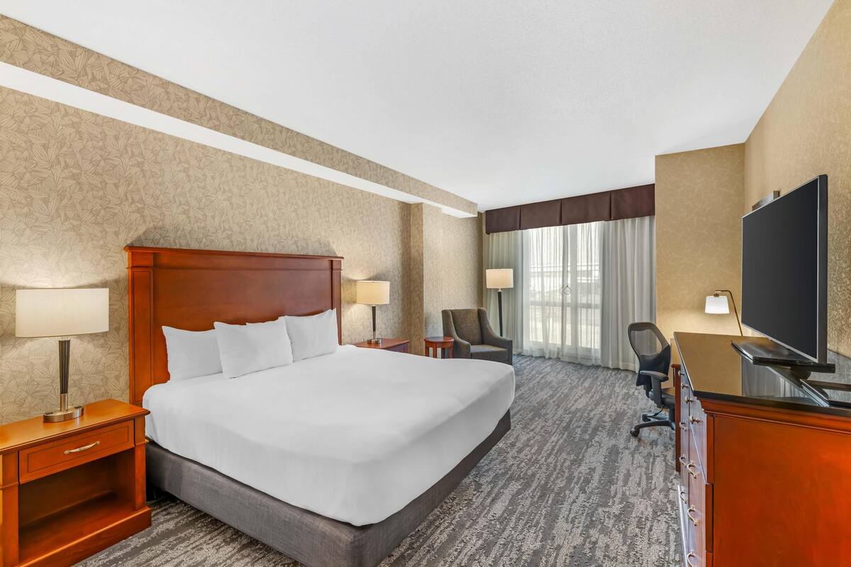 Una habitación de hotel con una cama grande, un escritorio con televisor, una silla y una lámpara.