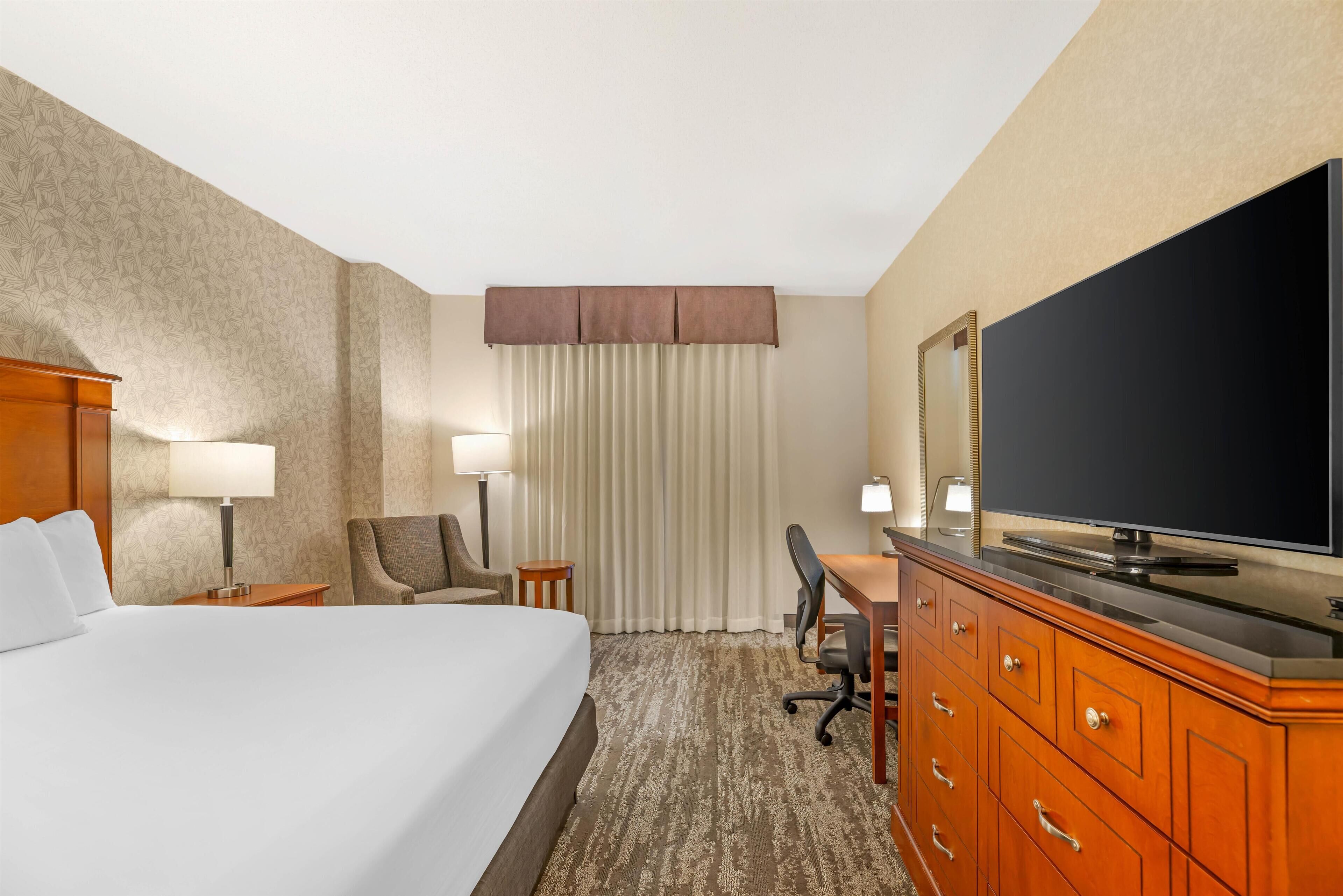 Ein Hotelzimmer mit einem großen Bett, einem Schreibtisch mit Stuhl, einem Fernseher und einem Kleiderschrank.