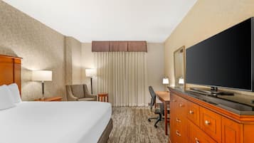 Ein Hotelzimmer mit einem großen Bett, einem Schreibtisch mit Stuhl, einem Fernseher und einem Kleiderschrank.