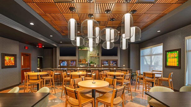 Un restaurante con mesas y sillas redondas, una zona de bar y un techo con diseño.