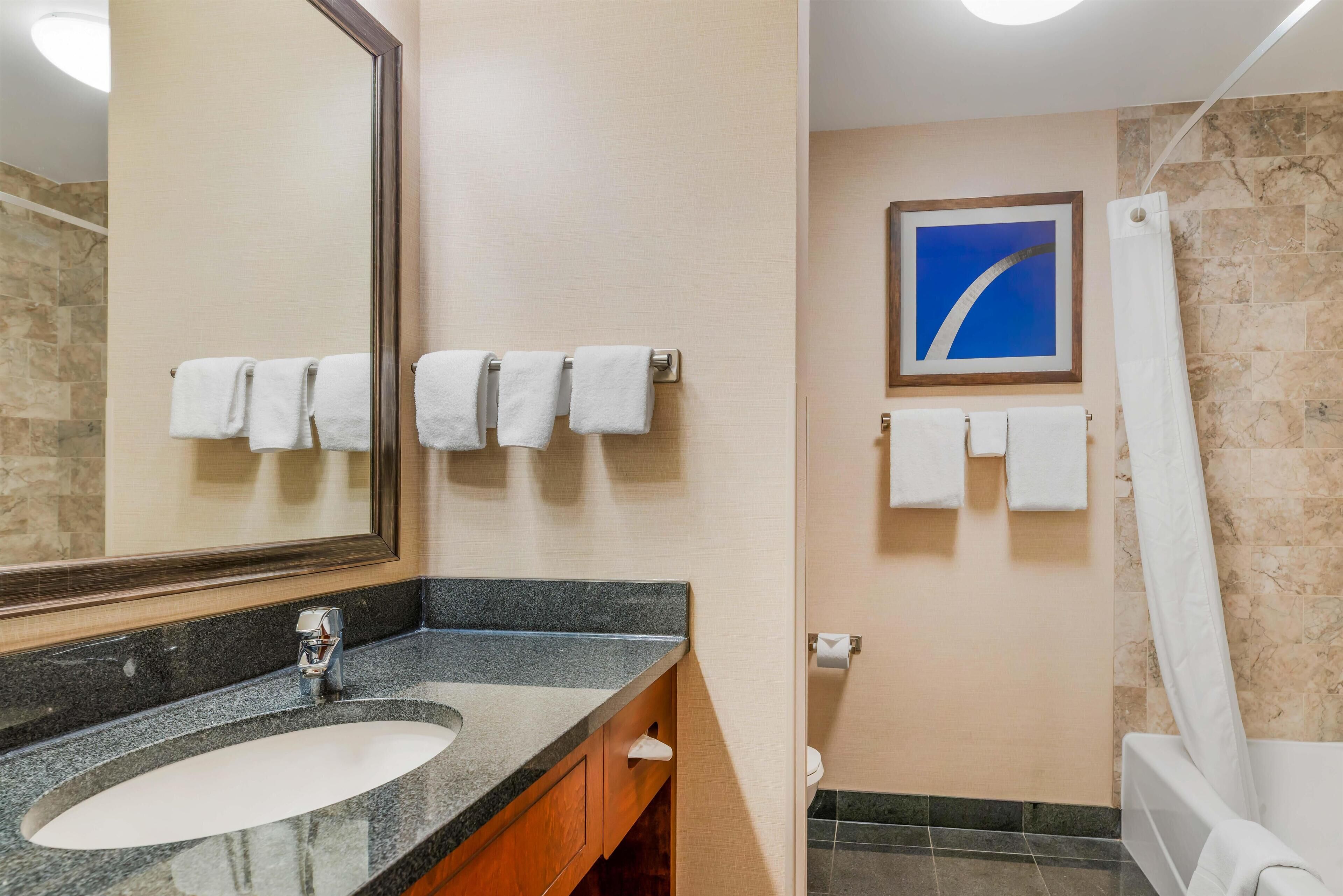 A bathroom with a granite countertop sink, a mirror, and a shower area.