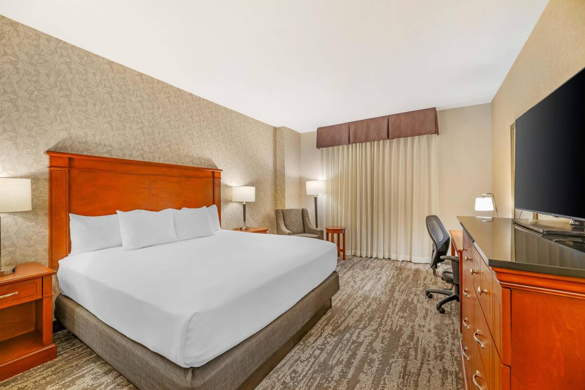 Habitación de hotel con una cama grande, dos mesitas de noche con lámparas, un escritorio con una silla y una televisión.
