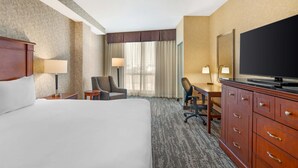 Una habitación de hotel con una cama grande, un escritorio con silla, televisión y armario.