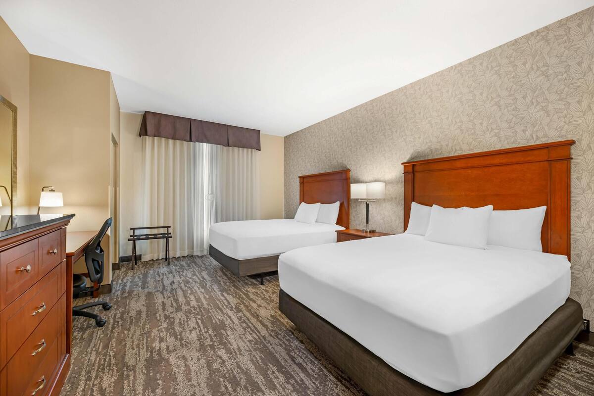 Una habitación de hotel con dos camas, un escritorio, una silla y un aparador.
