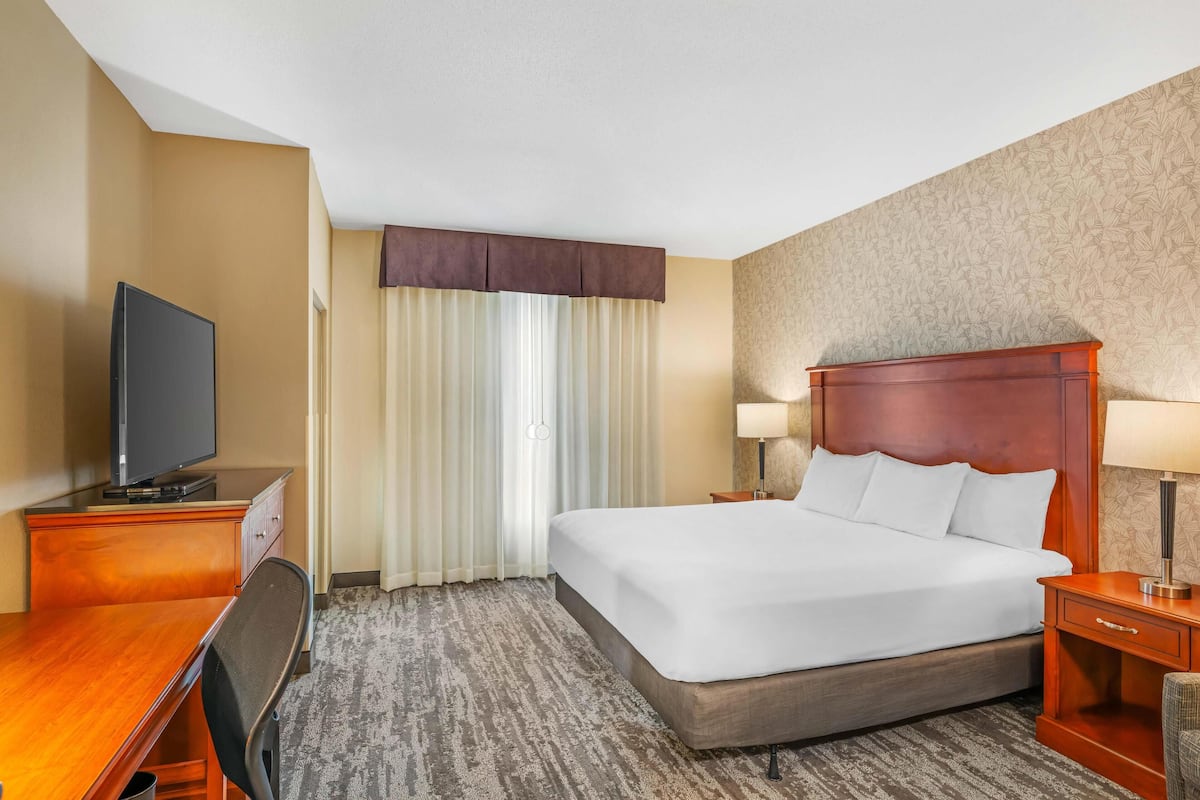 Una habitación de hotel con una cama grande, un escritorio con televisor, una lámpara y una silla.