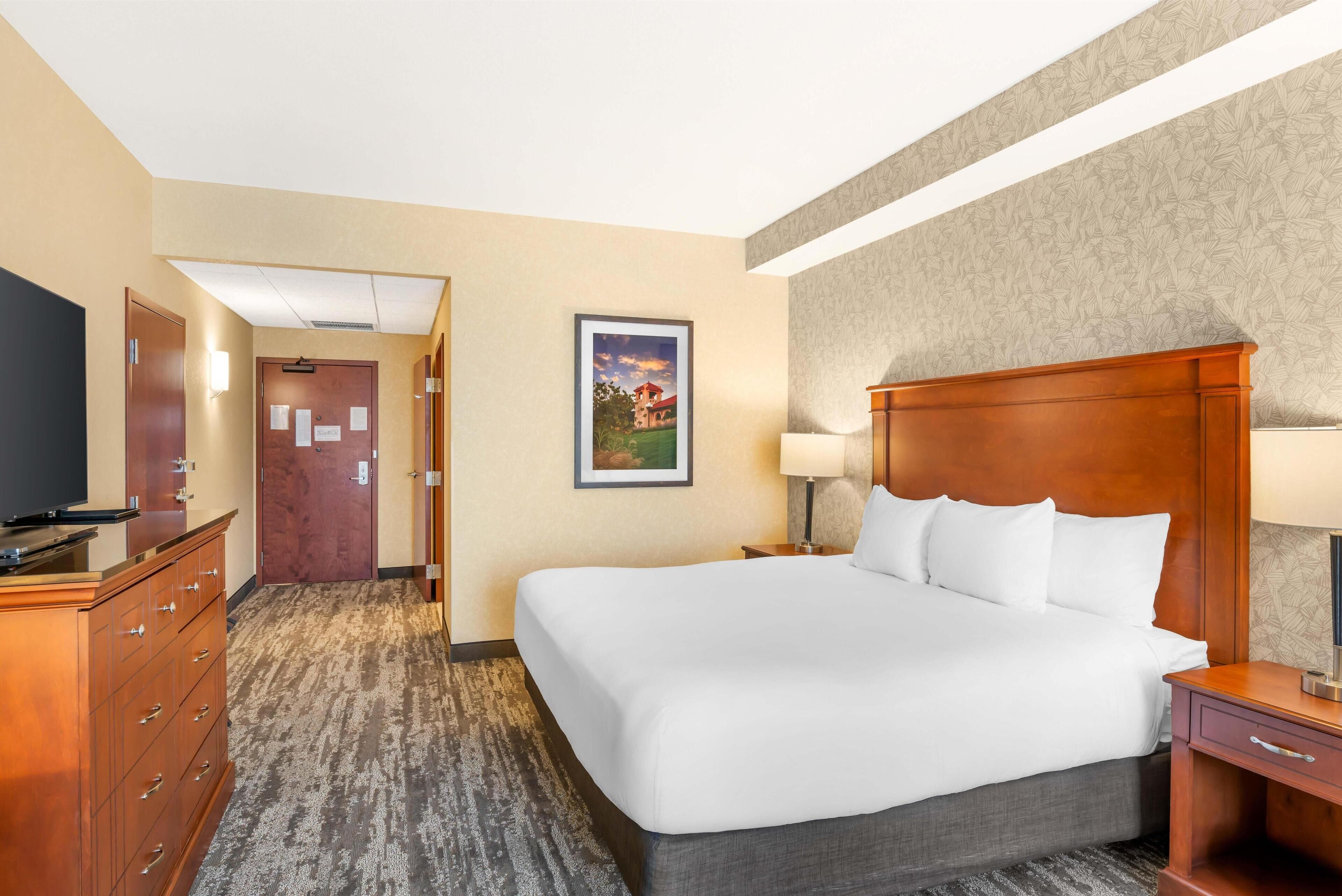 A hotel room with a large bed, a wooden dresser, a desk, and a television.