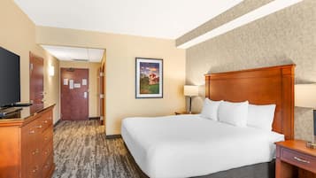 A hotel room with a large bed, a wooden dresser, a desk, and a television.