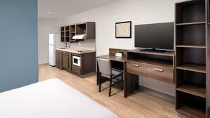 Una habitación de hotel moderna con cama, escritorio con silla, kitchenette, televisor y armario.