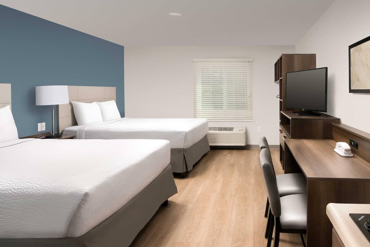 A hotel room with two beds, a desk, a chair, a television, and a window with blinds.
