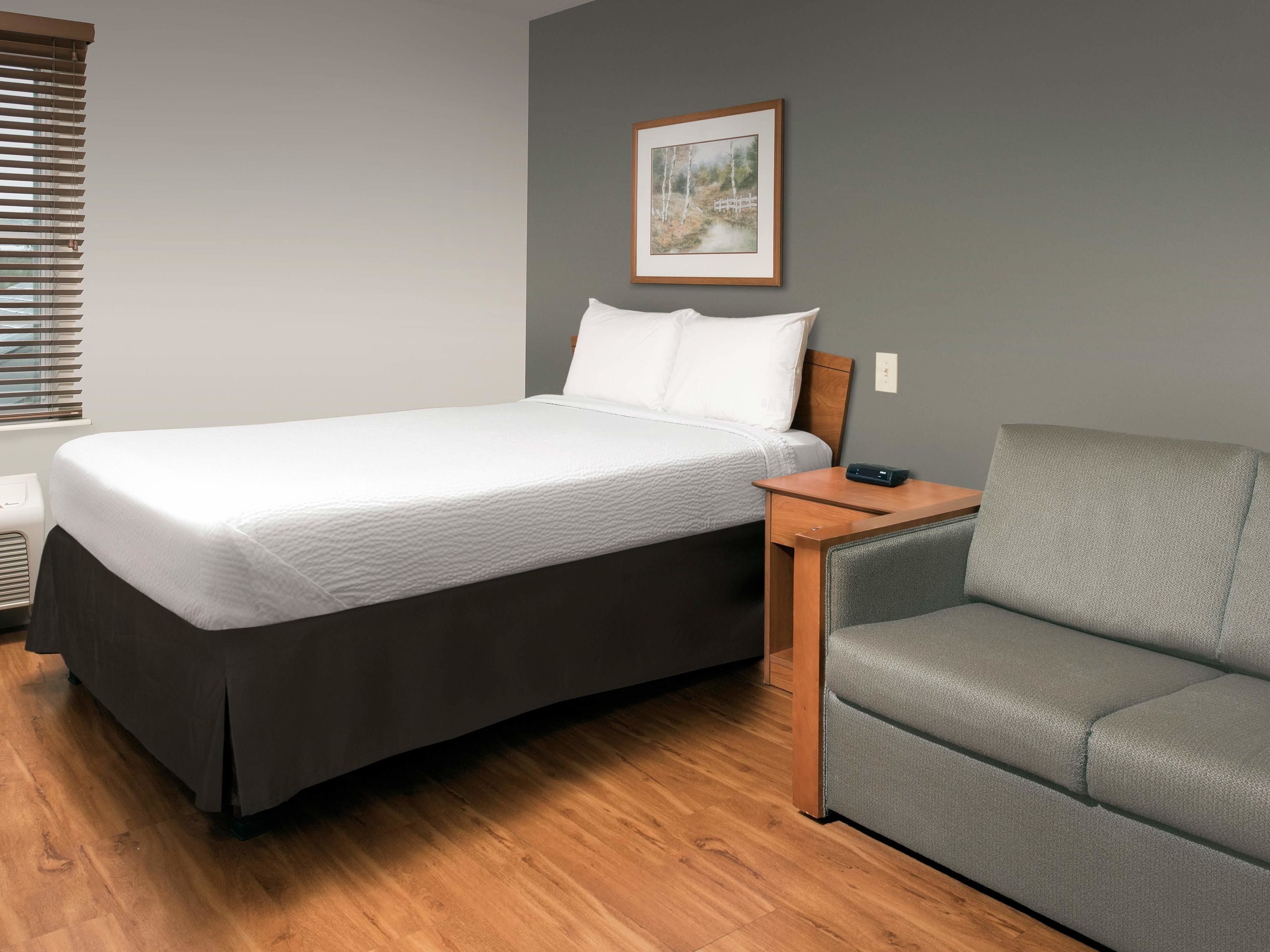 Une chambre à coucher bien rangée, avec un lit, un canapé gris et un tableau accroché au mur.
