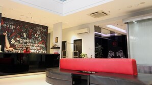 A modern lobby with a red seating area, a reception desk, and a large wall with motivational text. - G Suites Hotel by AMITHYA (Surabaya)