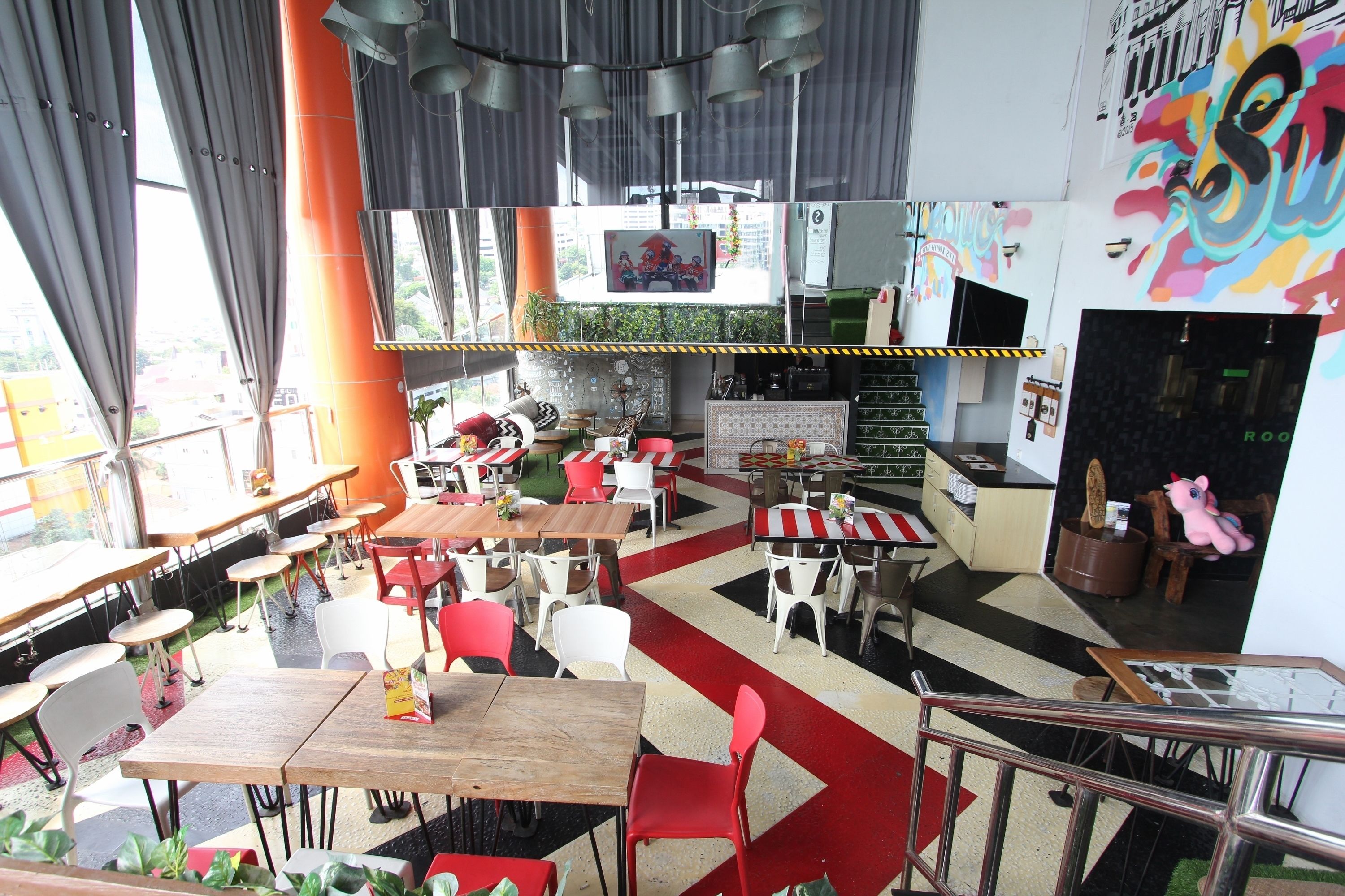 A restaurant with multiple tables and chairs, a large orange pillar, and a colorful mural on the wall.