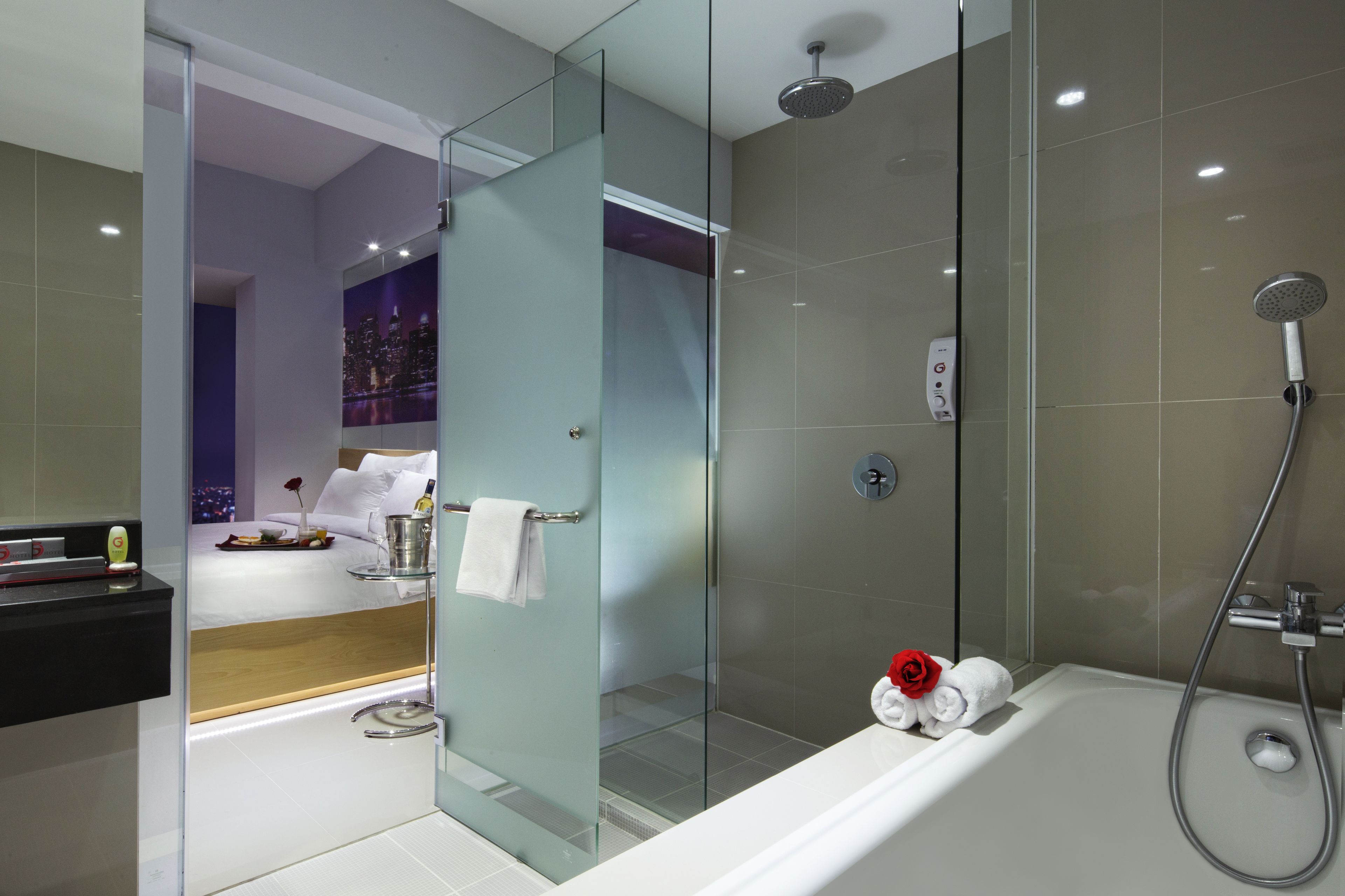 A modern bathroom with a glass-enclosed shower, a bathtub with a rose decoration, and a cityscape view through the glass door.