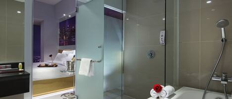 A modern bathroom with a glass-enclosed shower, a bathtub with a rose decoration, and a cityscape view through the glass door.