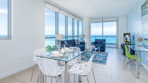 Ein modernes Wohnzimmer mit einem Glastisch, weißen Stühlen, einem blauen Sofa und Blick auf den Ozean.