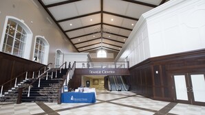 A spacious atrium with a high ceiling, a central staircase, and a table with a blue tablecloth.