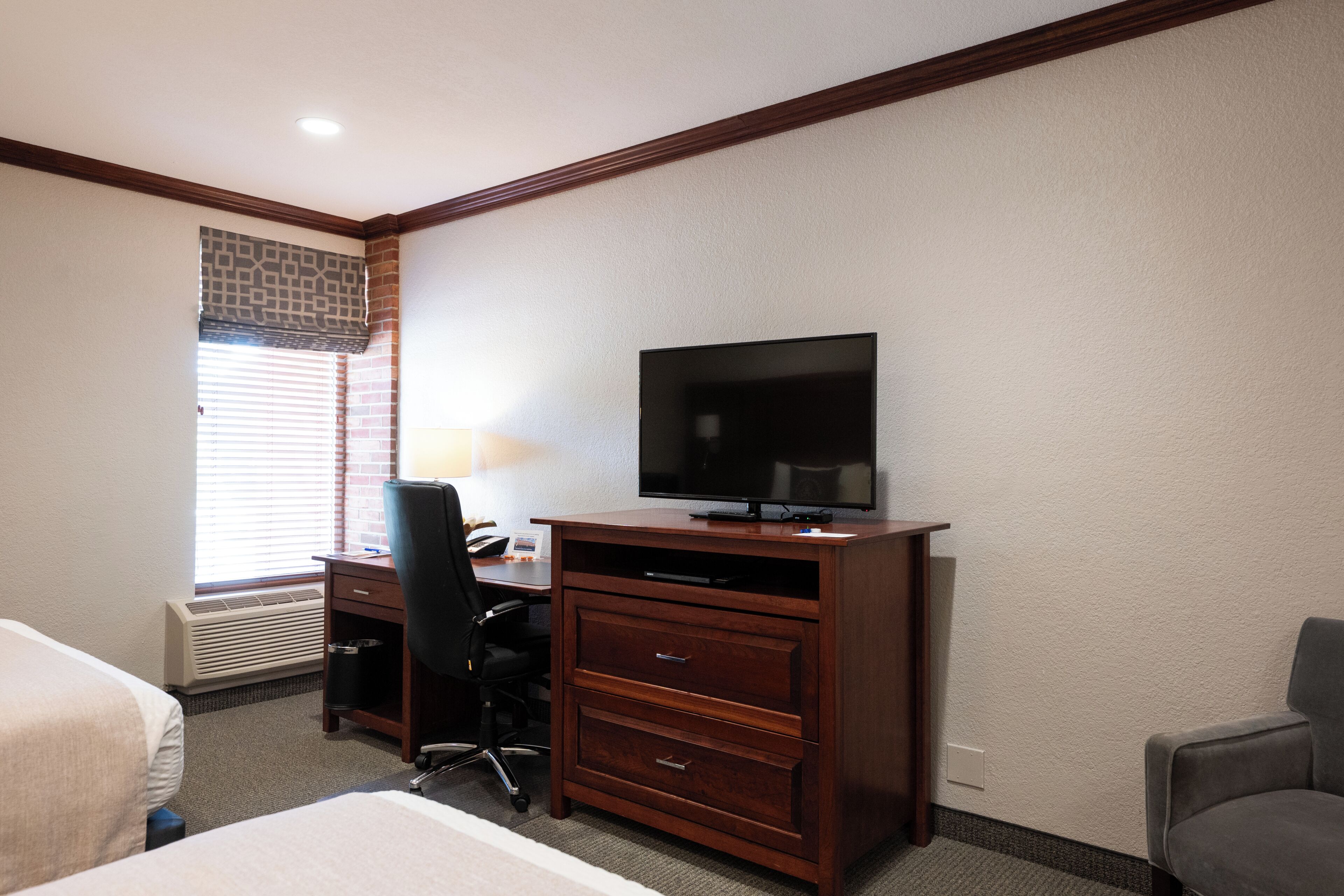 A hotel room with a bed, a desk with a chair, a television, and a window with blinds.