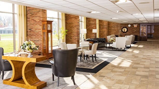 A spacious lobby with a brick wall, a large clock, and a seating area with a fireplace.