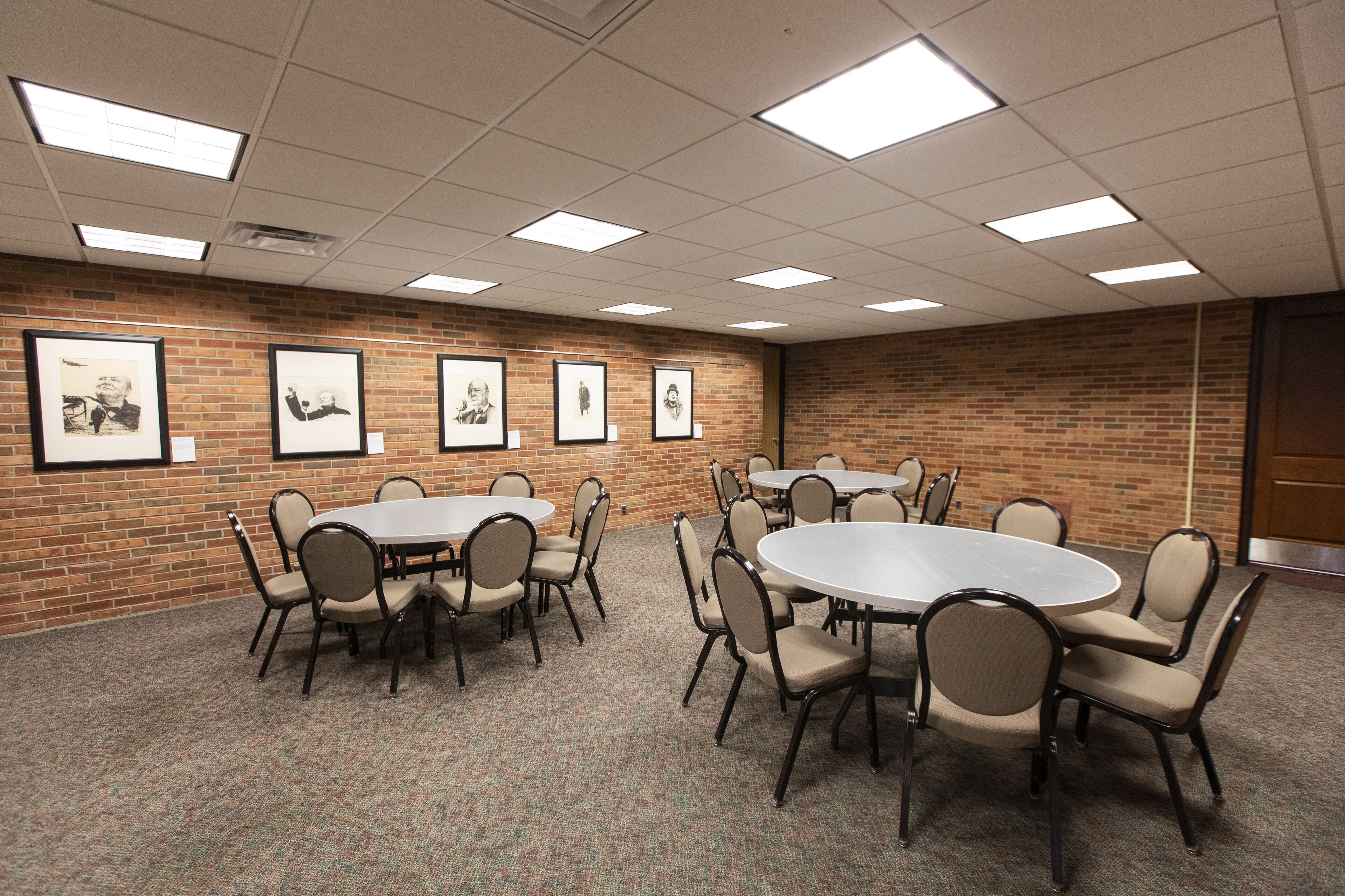 Uma sala de conferências com mesas e cadeiras redondas, parede de tijolos e quadros emoldurados.