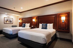 Quarto de hotel com duas camas, cabeceiras de madeira, abajures, um quadro na parede e chão coberto de carpete.