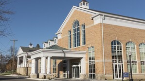 A large brick building with a central entrance, arched windows, and a covered porch area.