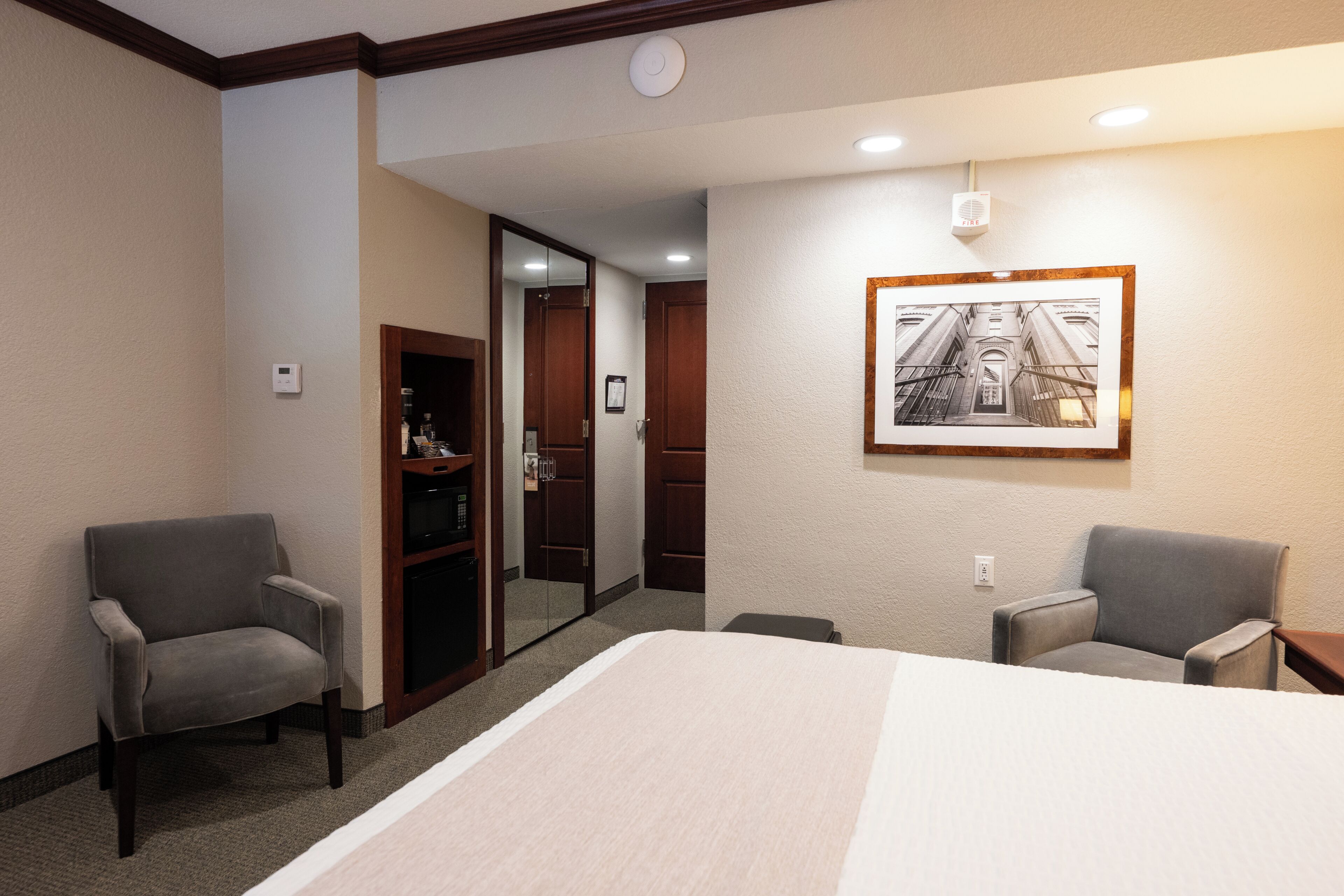 Habitación de hotel con una cama, dos sillones, un armario, un espejo y un cuadro en la pared.