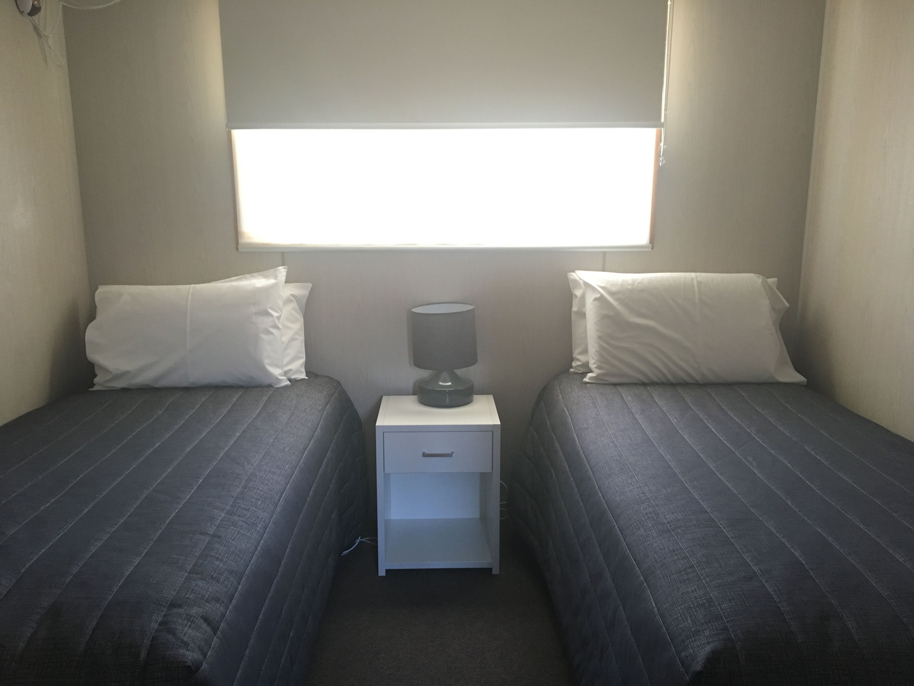 A small, simple room with two beds, a nightstand, and a window.