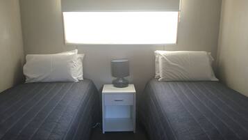A small, simple room with two beds, a nightstand, and a window.
