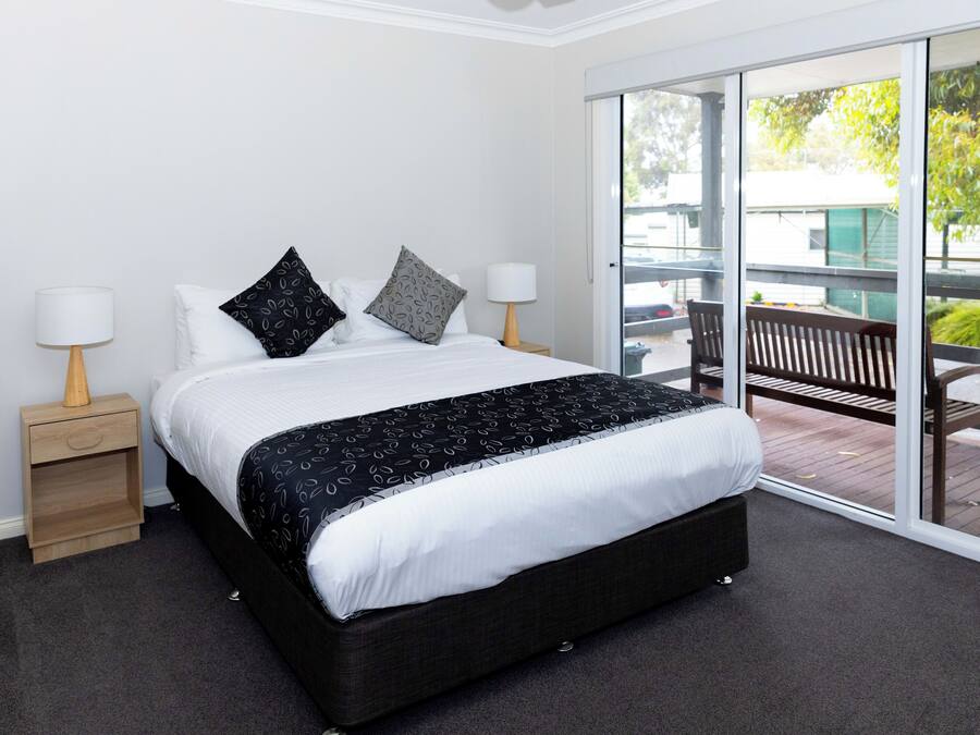 A bedroom with a large bed, two bedside tables with lamps, a sliding glass door leading to an outdoor area with a bench.