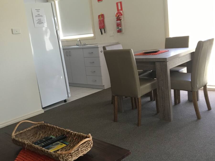 Ein Essbereich mit Holztisch und Stühlen, ein kleiner Korb auf einem Tisch sowie eine Küchenzeile mit Kühlschrank und Schränken.