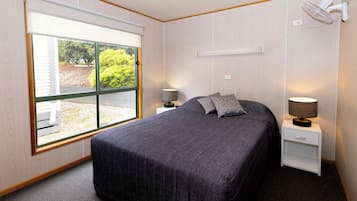 Un dormitorio con una cama grande, dos mesitas de noche con lámparas, una ventana con vistas a zonas verdes y un ventilador de techo.