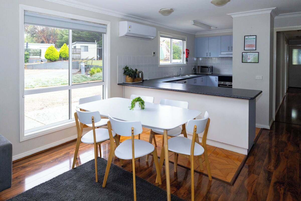 Una cocina moderna con armarios blancos, una isla central con asientos y un amplio ventanal con vistas al exterior.