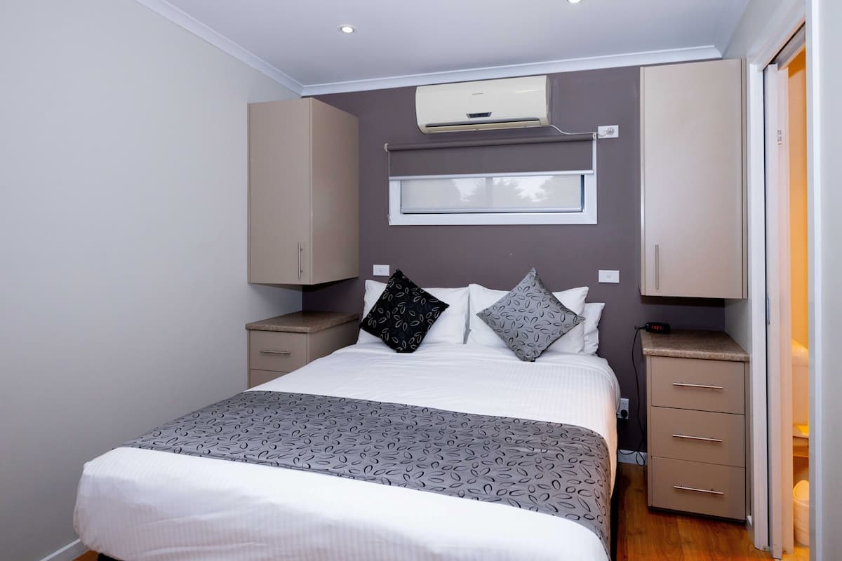 Un dormitorio con cama, mesitas de noche, aire acondicionado, ventana y armario.