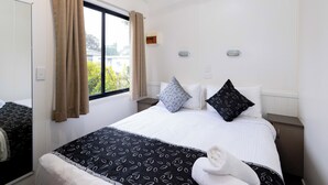 Una habitación de hotel con cama, ventana con cortinas, mesita de noche y espejo.