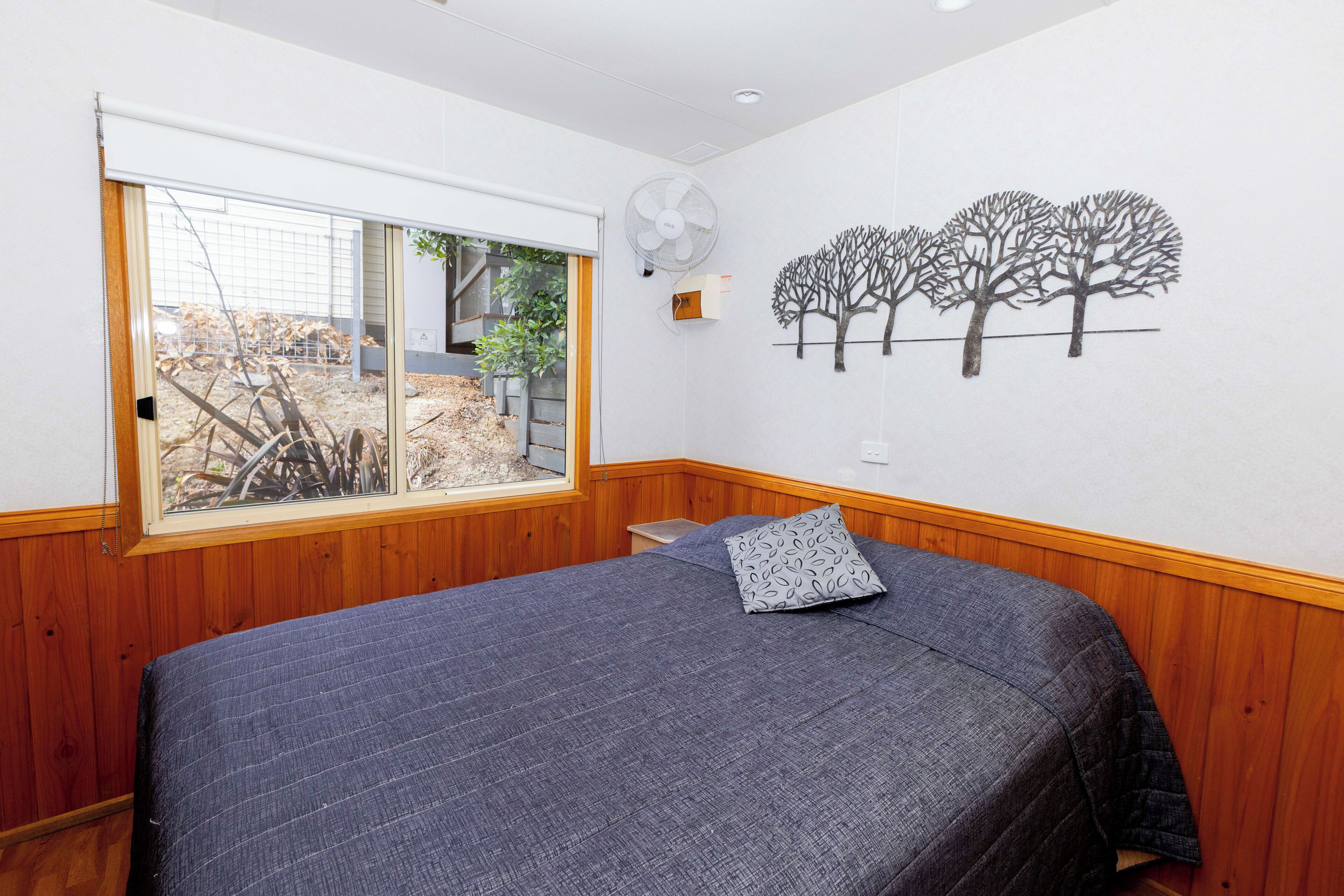 A bedroom with a bed, a window, a fan, and a wall mural.