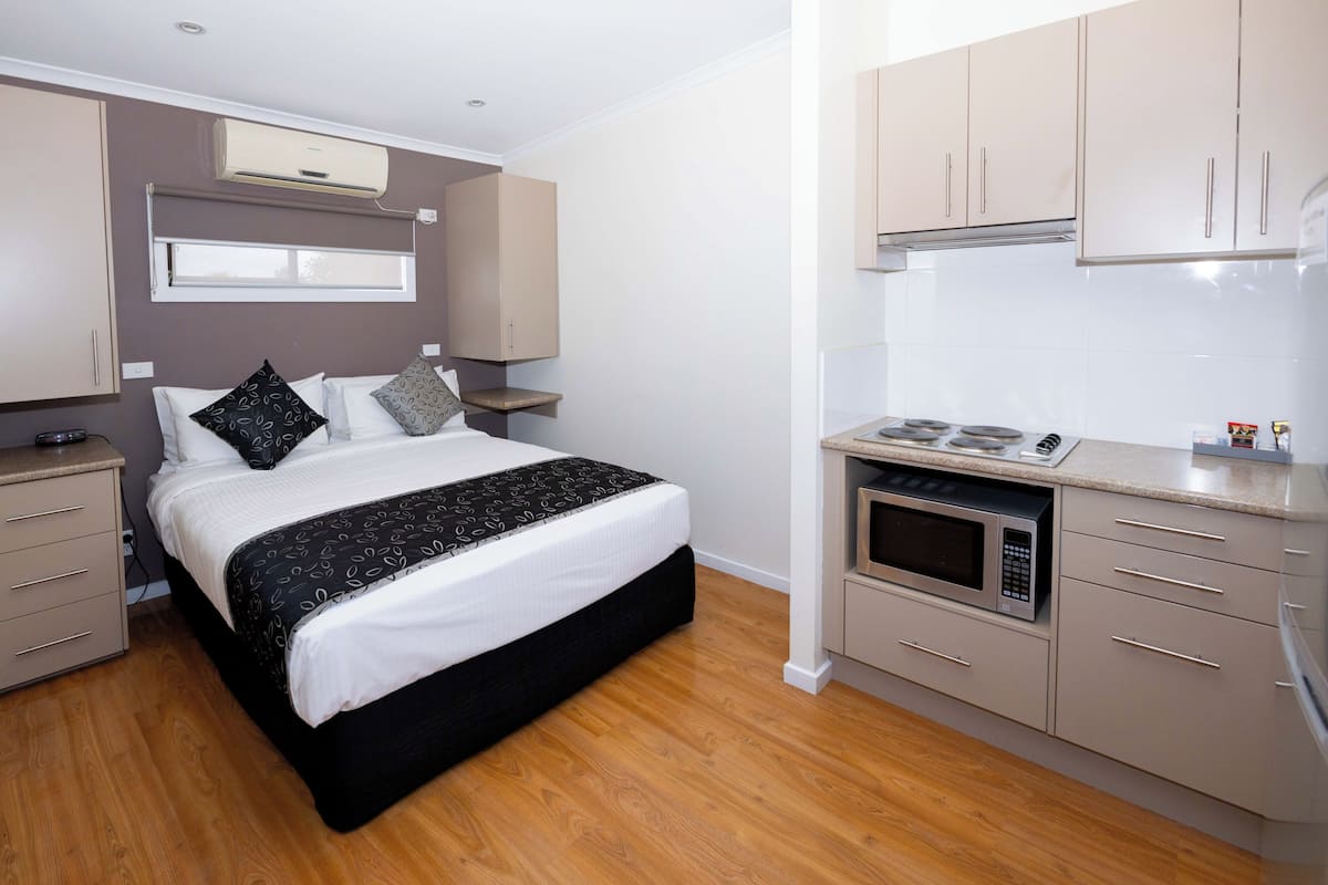 Un dormitorio con cama, mesitas de noche, microondas integrado y una kitchenette con armarios.