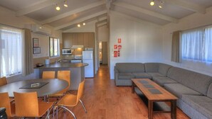 Una sala de estar moderna con un sofá, una mesa de comedor y sillas. Cuenta con una zona de cocina con microondas y refrigerador.