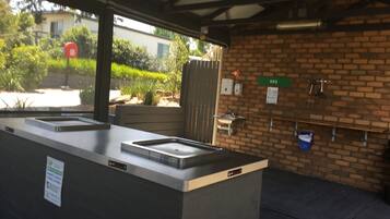 Un espacio al aire libre techado con pared de ladrillo, un lavamanos y un letrero de barbacoa.