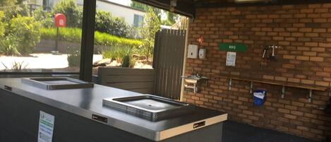 A covered outdoor area with a brick wall, a sink, and a BBQ sign.