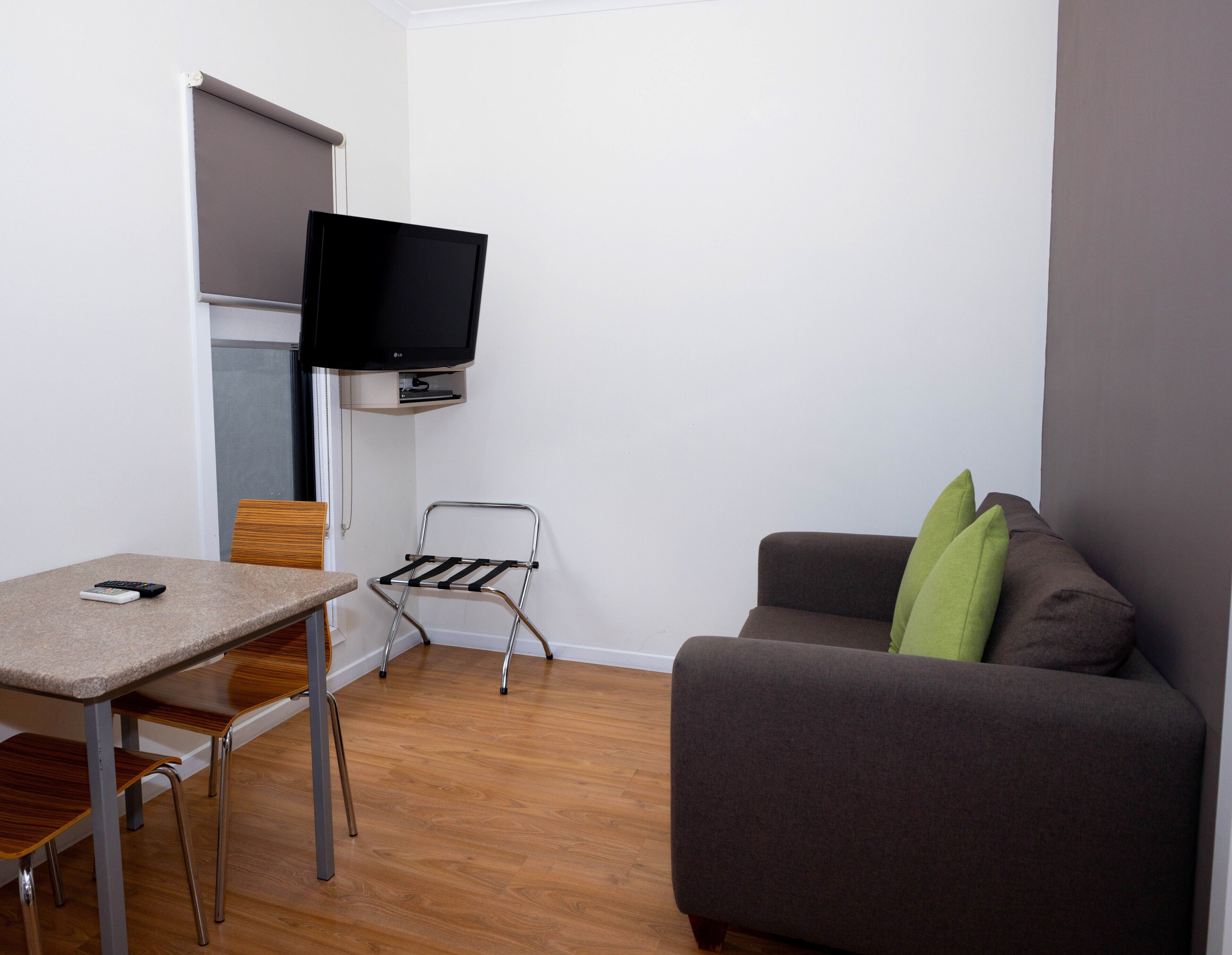 Un espacio habitable compacto con una televisión de pantalla plana montada en la pared, una mesita con una silla, un tendedero metálico y un sofá con cojines.