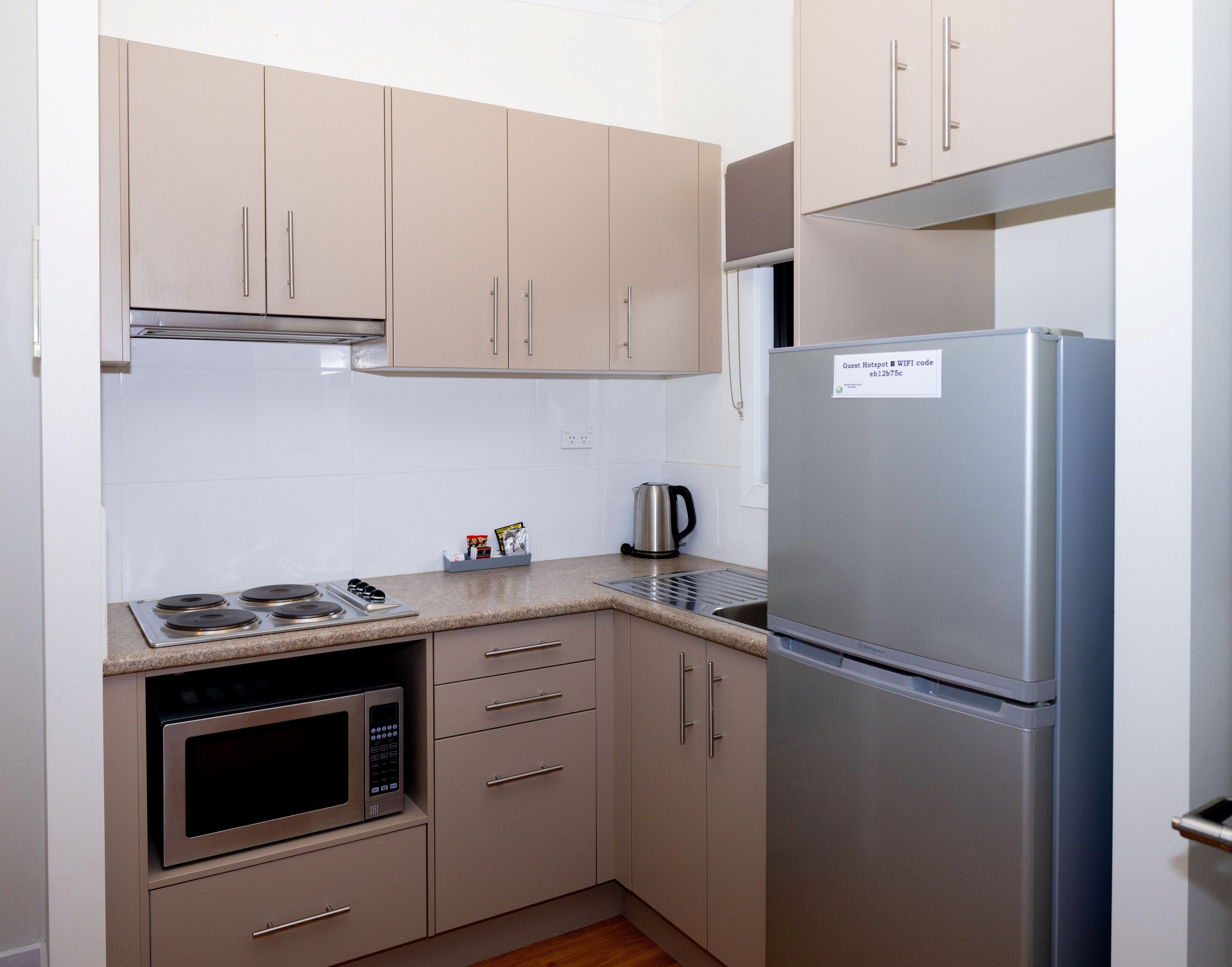 A compact kitchen with beige cabinets, a stainless steel refrigerator, a microwave, and a gas stove.