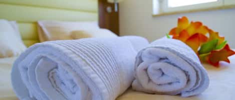 A neatly made bed with rolled white towels and a bouquet of orange and red flowers.