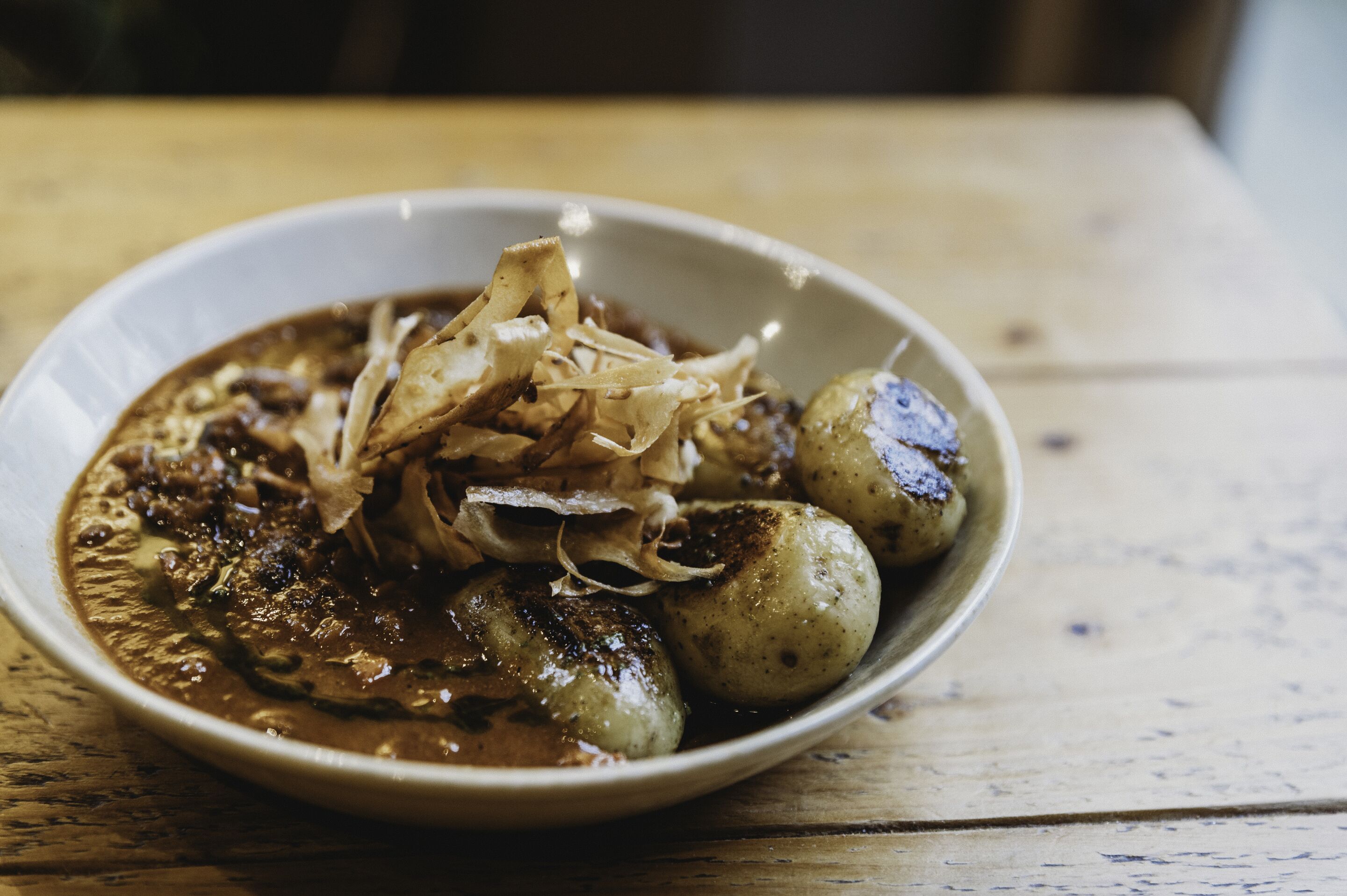 A bowl of food with potatoes and a sauce, served on a wooden table.