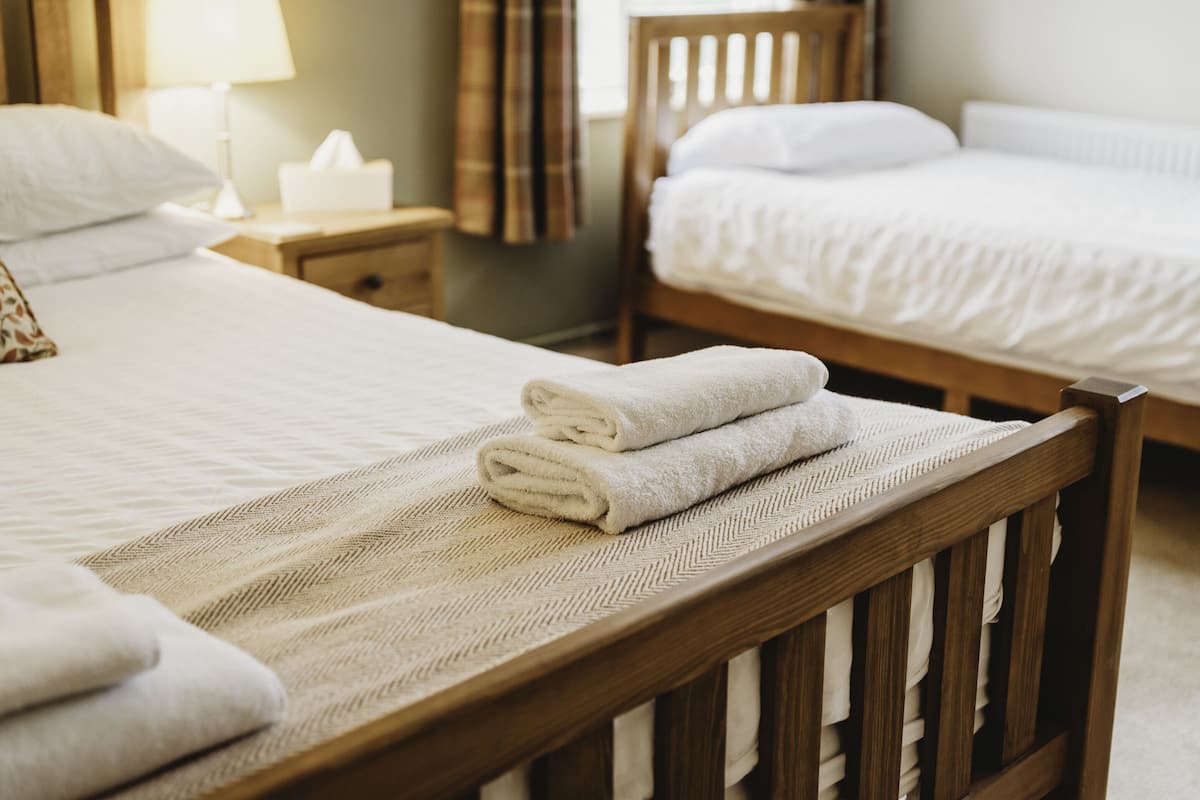 A neatly made bed with folded towels, a bedside table with a lamp, and a wooden headboard.