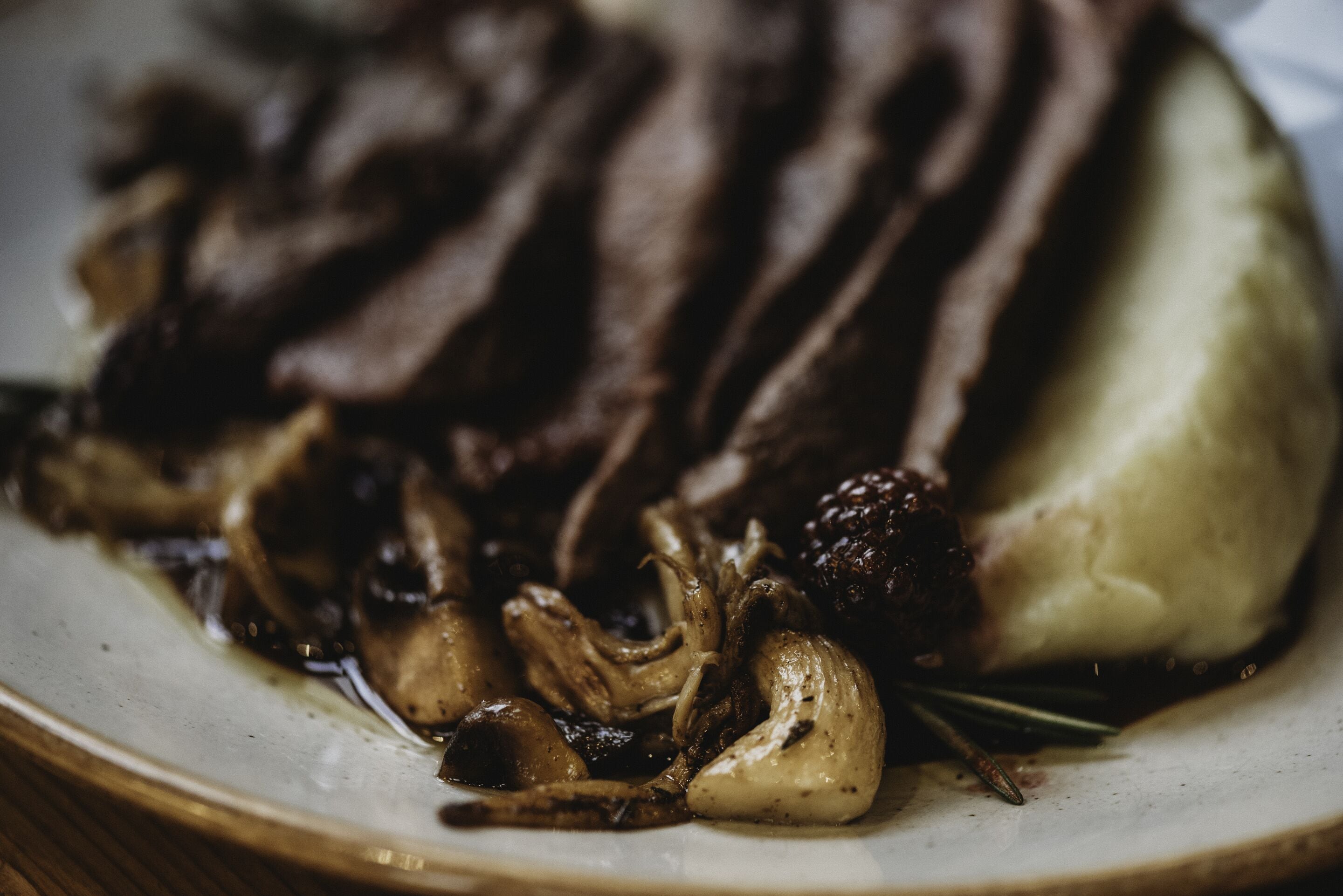 Une assiette contenant de la viande en tranches, des champignons et de la purée de pommes de terre.
