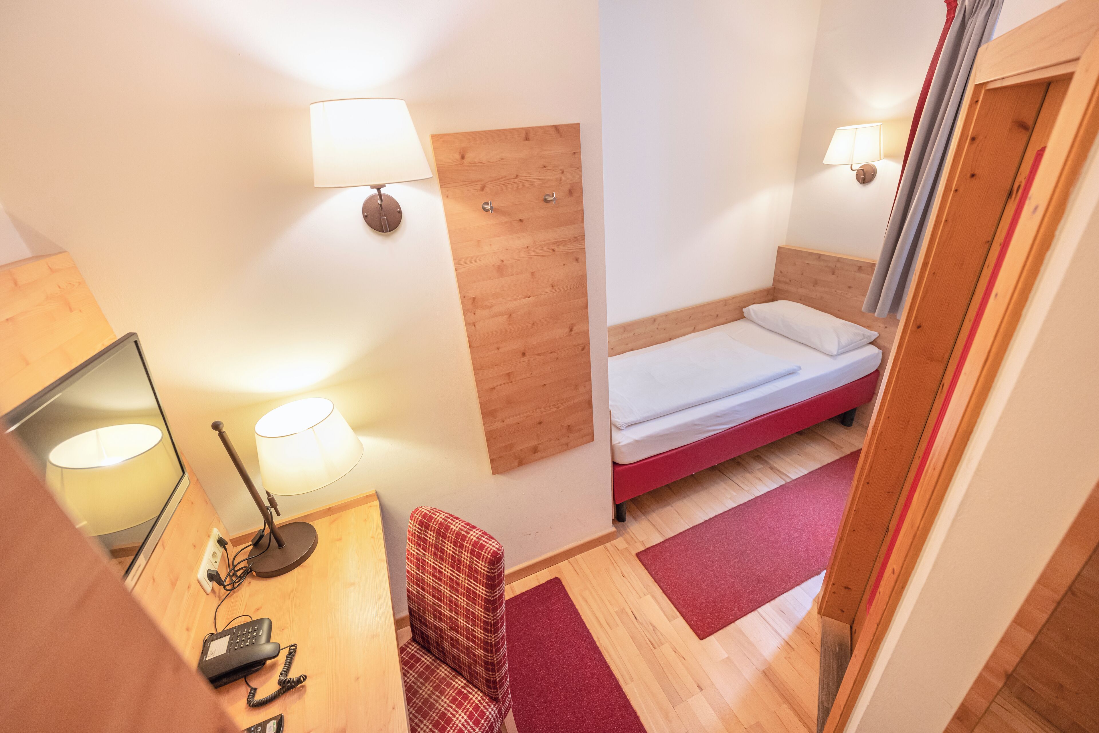 Ein Hotelzimmer mit Holzkopfende, einem Bett mit weißer Bettwäsche, einem Schreibtisch mit Lampe und einem Stuhl.
