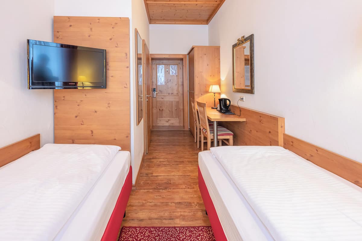 Una camera d'albergo con due letti, una TV, una scrivania con lampada e uno specchio.