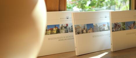 Dos libros titulados 'BEGEGNUNGEN IN MÜNCHEN GIESING UND HARLACH' sobre una mesa de madera cerca de una ventana.