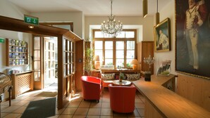 A lobby with a wooden reception desk, red armchairs, a chandelier, and a large window. - Eder  (Munich)