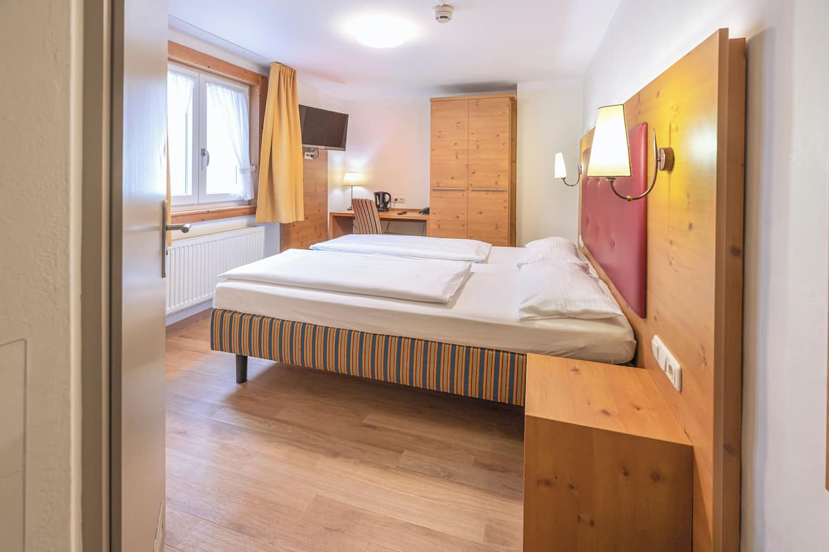 Una camera d'albergo con un letto, un armadio in legno, una scrivania con una sedia e una finestra con tende.